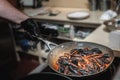 The cook`s hand holds a pan with cooking mussels. Fresh mussels are cooked in a pan in a delicious creamy wine sauce. close-up of Royalty Free Stock Photo