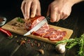 Cook's hands cut with a knife grilled beef meat on a cutting board. Work environment on the kitchen table with condiments or Royalty Free Stock Photo
