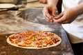 Cook`s hands putting salsiccia sausage on tomato base pizza. Royalty Free Stock Photo