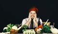 Cook sits in kitchen near table with vegetables and tools. Cuisine and professional cooking. Man in burgundy hat and Royalty Free Stock Photo