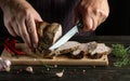 The cook slicing grilled beef meat on a cutting board. Work environment on the kitchen table with condiments or spices. Dark Royalty Free Stock Photo