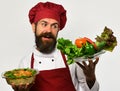 Cook with smile in burgundy uniform holds dish and salad.