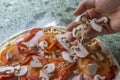The cook sprinkles raw pizza with pieces of mushrooms mushrooms