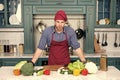 Cook stand at kitchen table. Man in chef hat and apron in kitchen. Vegetables and tools ready for cooking dishes