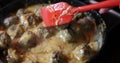 Cook stirs meatballs in creamy sauce in pan