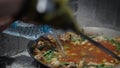 The cook stirs the paella while the helper pours water