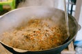 The cook stirs pilaf in the cauldron.