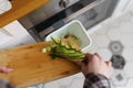 Cook throwing cucumber peels in a bokashi container for decomposition. Female person recycling organic food waste in a compost bin