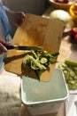 Cook throwing cucumber peels in a compost bin. Woman cooking fresh green salad at home and composting organic waste in a bokashi