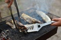 The cook turns the baked fish on the net with a metal spatula