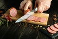 The cook uses a knife to cut salami sausage into thin slices for a sandwich. Low key concept of fast food cooking with spices on Royalty Free Stock Photo