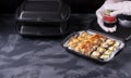 Cook wearing disposable gloves is packing sushi rolls into the black container.