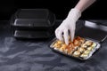 Cook wearing disposable gloves is packing sushi rolls into the black container.