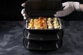 Cook wearing disposable gloves is packing sushi rolls into the black container