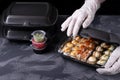 Cook wearing disposable gloves is packing sushi rolls into the black container