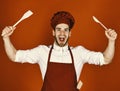 Cook works in kitchen. Chef with excited face holds wooden spoon and spatula on red background. Kitchenware and cooking Royalty Free Stock Photo
