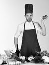 Cook works in kitchen near table with vegetables and tools. Cuisine and cooking concept. Man in cook hat and apron Royalty Free Stock Photo