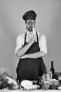 Cook works in kitchen near table with vegetables and tools. Man in cook hat and apron looks through radish Royalty Free Stock Photo