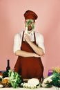 Cook works in kitchen near table with vegetables and tools. Man in cook hat and apron looks through radish Royalty Free Stock Photo