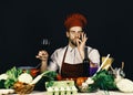 Cook works in kitchen near vegetables and tools. Italian drink and sommelier concept. Man in hat and apron Royalty Free Stock Photo