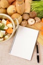 Cookbook or notepad with casserole dish and organic vegetables on kitchen worktop, copy space, vertical Royalty Free Stock Photo