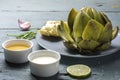 Cooked artichoke with dips and bread on rustic gray blue wood