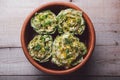 Cooked artichokes with parsley and parmesan, served in a clay dish on a wooden table