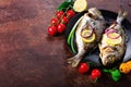 Cooked baked grilled fish, dorado, sea bream with lemon, herbs, vegetables and spices on rustic background. Top view