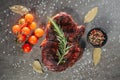 Cooked beef steak on a dark metal cutting board, next to a sprig of aromatic rosemary, tomatoes, a black pot of peppercorn mix and Royalty Free Stock Photo