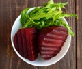 Cooked beets and arugula in a white bowl.