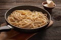Cooked cacio pepe pasta in a skillet with pecorino cheese on wooden background