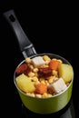 Cooked Cocido, Guiso stew, chickpeas with chorizo, bacon, carrot and potato in a green saucepan and on a black background.