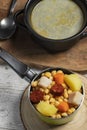 Cooked Cocido, Guiso stew, chickpeas with chorizo, bacon, carrot and potato in green saucepan, black casserole with broth and on