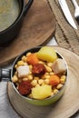 Cooked Cocido, Guiso stew, chickpeas with chorizo, bacon, carrot and potato in green saucepan, black casserole with broth and on