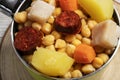 Cooked Cocido, Guiso stew, chickpeas with chorizo, bacon, carrot and potato in a green saucepan and on wooden board. Concept of