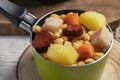 Cooked Cocido, Guiso stew, chickpeas with chorizo, bacon, carrot and potato in a green saucepan and on wooden board. Concept of