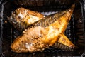 Cooked headless mackerel in a black plastic container