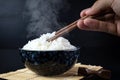 Cooked jasmine rice in ceramic cups and chopsticks holding hot jasmine rice with hand. Placed on a black wooden table. Close up Royalty Free Stock Photo