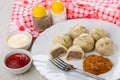 Cooked khinkali, squash caviar, fork in plate, salt, pepper, sauces in bowls, napkin on wooden table