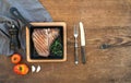 Cooked meat t-bone steak with garlic cloves, tomatoes, rosemary, pepper and salt in small cooking pan over rustic wooden Royalty Free Stock Photo