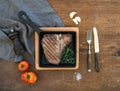 Cooked meat t-bone steak with garlic cloves, tomatoes, rosemary, pepper and salt in small cooking pan over rustic wooden Royalty Free Stock Photo