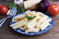 Cooked penne pasta with butter,cheese and fresh vegetable ingredients on background: tomato, garlic, onion, fork and spoon, basil.