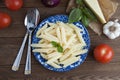 Cooked penne pasta with butter,cheese and fresh vegetable ingredients on background: tomato, garlic, onion, fork and spoon, basil.