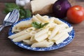 Cooked penne pasta with butter,cheese and fresh vegetable ingredients on background: tomato, garlic, onion, fork and spoon, basil.