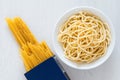 Cooked spaghetti in a white ceramic bowl next to uncooked spaghetti in a blue box on white painted wood Royalty Free Stock Photo