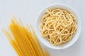 Cooked spaghetti in a white ceramic bowl next to uncooked spaghetti on white painted wood Royalty Free Stock Photo