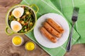 Vegetable mix, boiled egg in bowl, knife, salt shaker, pepper shaker, fried sausages in plate, fork on napkin on table. Top view Royalty Free Stock Photo