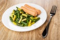 Cooked yellow and green beans with sausages in plate, fork on table