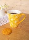 A cookie and a yellow cup of coffee and daisies in the background Royalty Free Stock Photo