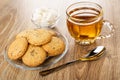Cookies with flax seeds, sesame in saucer, sugar in bowl, transparent cup with tea, spoon on wooden table Royalty Free Stock Photo